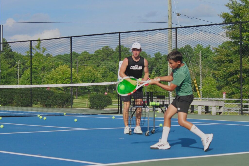 An ATA coach feeding forehands to a junior player during a lesson
