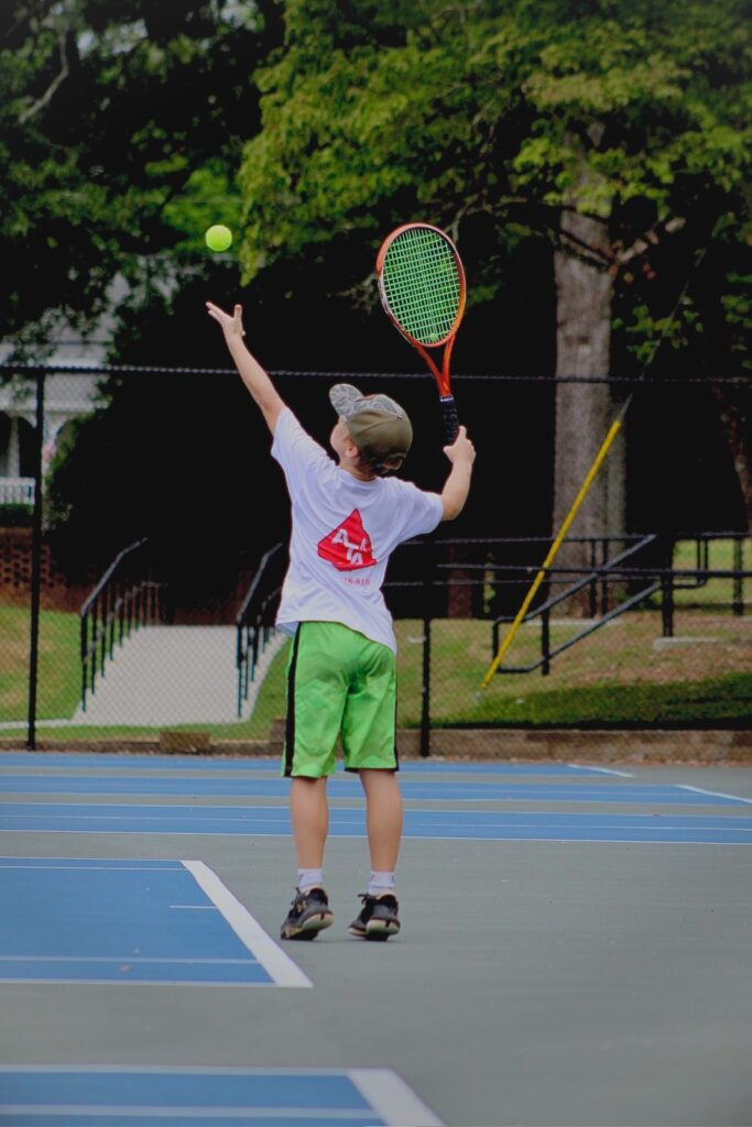 A junior player tossing up a serve in an ATA shirt