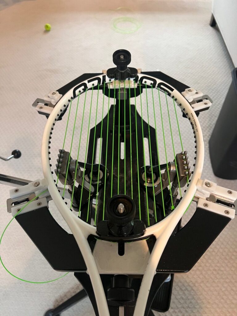A racket being strung with bright green string on a stringing machine